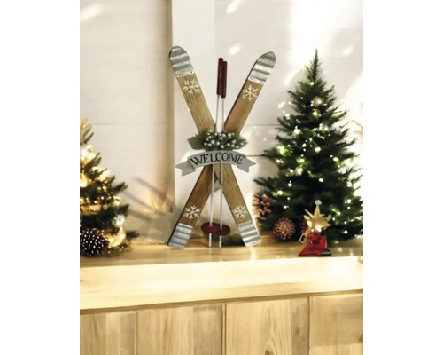 Dekorative Holzskier in Form eines X mit Welcome Schild zwischen zwei kleinen beleuchteten Weihnachtsbäumen auf einer hellen Holzfläche.