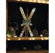 Weihnachtsdekoration aus Holz in Form von gekreuzten Skiern mit Skistöcken, Welcome-Schild, Schneeflocken und Tannenzapfen auf einem Regal.
