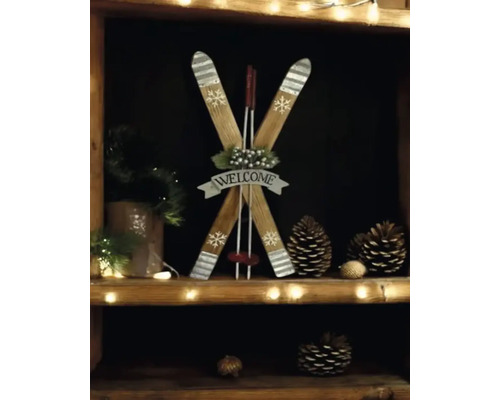 Weihnachtsdekoration aus Holz in Form von gekreuzten Skiern mit Skistöcken, Welcome-Schild, Schneeflocken und Tannenzapfen auf einem Regal.