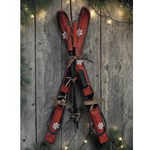 Dekorative Holzski und Skistöcke mit Schneeflocken-Muster vor rustikaler Holzwand mit Tannenzweigen und Lichterkette.