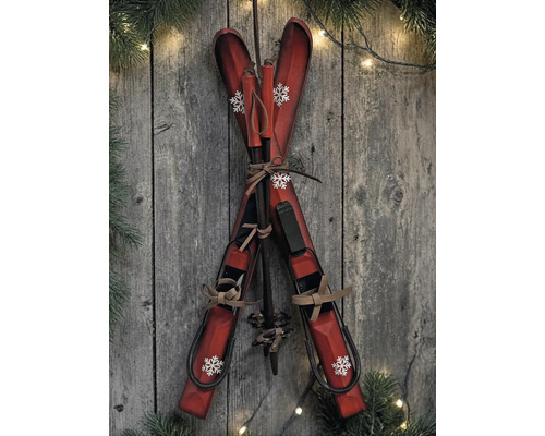Dekorative Holzski und Skistöcke mit Schneeflocken-Muster vor rustikaler Holzwand mit Tannenzweigen und Lichterkette.