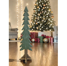 Dekorativer Weihnachtsbaum aus Holz auf einem Standfuß vor einem geschmückten Christbaum mit Geschenken in einem hellen Wohnzimmer.