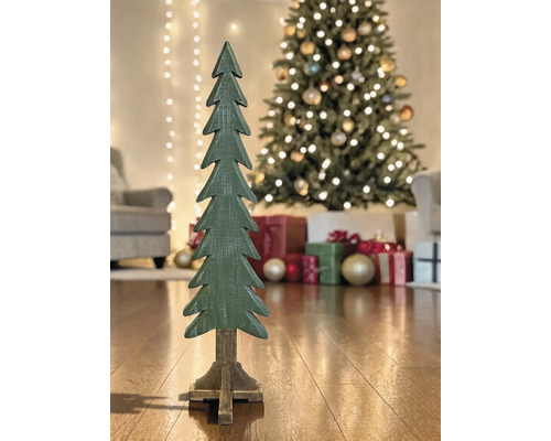 Dekorativer Weihnachtsbaum aus Holz auf einem Standfuß vor einem geschmückten Christbaum mit Geschenken in einem hellen Wohnzimmer.