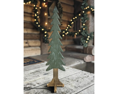 Grüner dekorativer Tannenbaum aus Holz auf einem Holzständer in rustikaler Umgebung mit Beleuchtung.