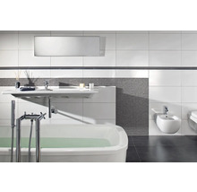 Salle de bains moderne avec baignoire blanche, lavabo suspendu et bidet, mosaïque grise et grands carreaux muraux blancs.