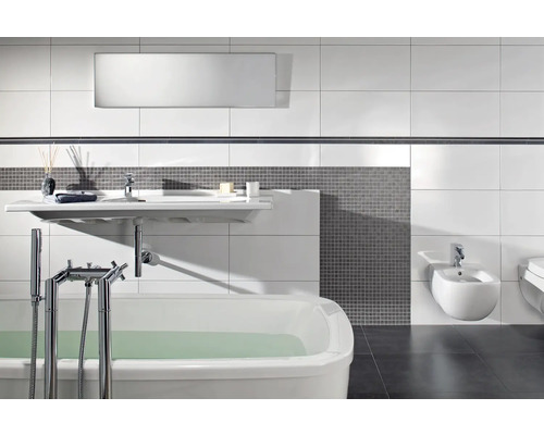 Salle de bains moderne avec baignoire blanche, lavabo suspendu et bidet, mosaïque grise et grands carreaux muraux blancs.