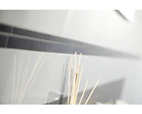 Gros plan de carreaux de mur blancs brillants avec une frise foncée et texturée.