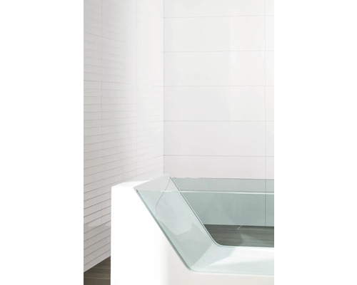 Baignoire moderne avec paroi latérale en verre devant un fond carrelé blanc.