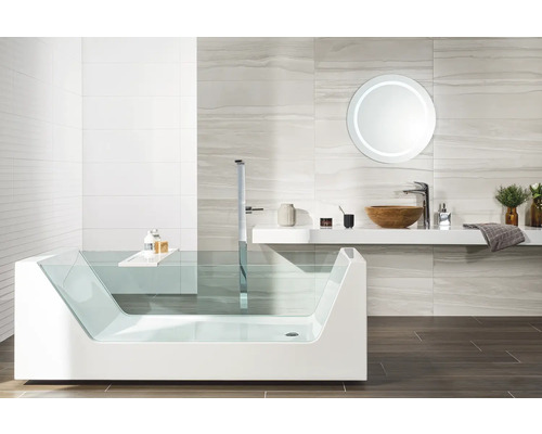 Salle de bains moderne avec baignoire en verre, robinetterie sur pied, vasque en bois et miroir rond rétroéclairé.