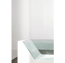 Baignoire moderne avec paroi latérale en verre devant un fond carrelé blanc.