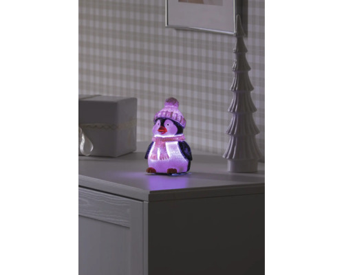 Pingouin décoratif à LED avec bonnet et écharpe, illuminé sur un buffet à côté d'un sapin décoratif et d'un cadeau.