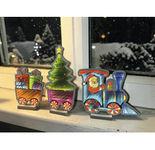 Décoration train de Noël en trois pièces sur un rebord de fenêtre avec locomotive, Père Noël, sapin et cadeaux devant une fenêtre hivernale.