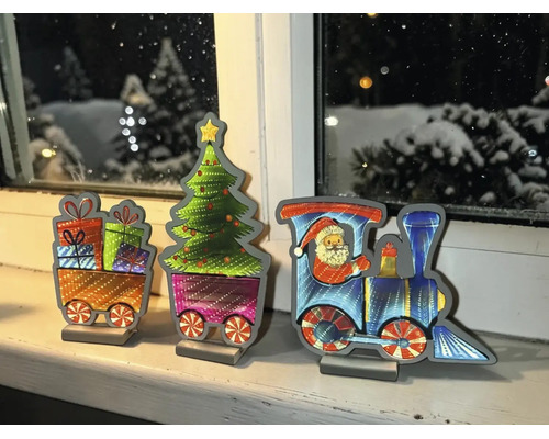 Décoration train de Noël en trois pièces sur un rebord de fenêtre avec locomotive, Père Noël, sapin et cadeaux devant une fenêtre hivernale.