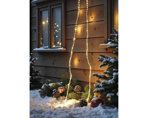 Warmweiße LED-Lichterkette an einer Holzwand mit verschneiten Tannenzweigen und Zapfen im Vordergrund.