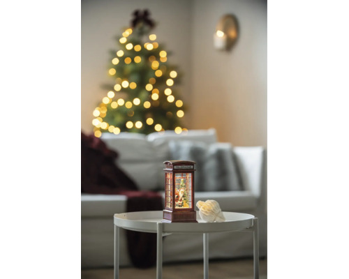 LED-Wasserlaterne in Form einer Telefonzelle mit Weihnachtsmannfigur auf einem Tisch in einem hell beleuchteten Wohnzimmer.