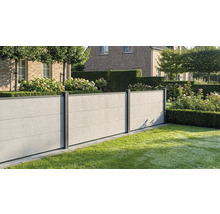 Clôture moderne aspect béton avec poteaux sombres dans un jardin soigné avec pelouse, haies et hortensias devant une maison en briques.