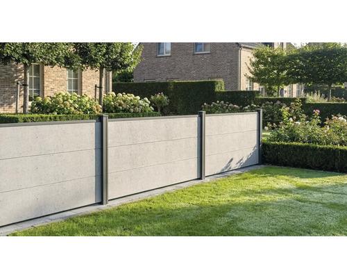 Clôture moderne aspect béton avec poteaux sombres dans un jardin soigné avec pelouse, haies et hortensias devant une maison en briques.