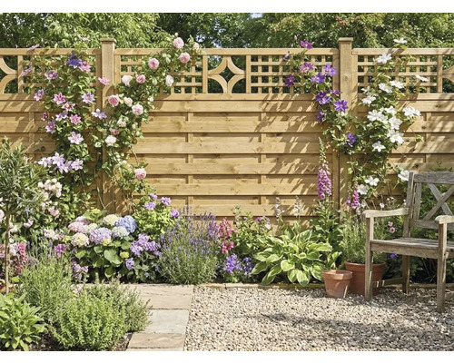 Clôture de jardin en bois avec treillis, couverte de rosiers grimpants et clématites, massif de fleurs avec hortensias, lavande et chaise en bois.