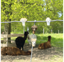 Zaunfiguren in Alpaka-Form an einem Drahtzaun vor einer Weide mit echten Alpakas.