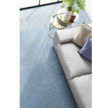 Strukturierter blauer Teppichboden in einem hellen Wohnzimmer mit grauem Sofa und gläsernem Beistelltisch.