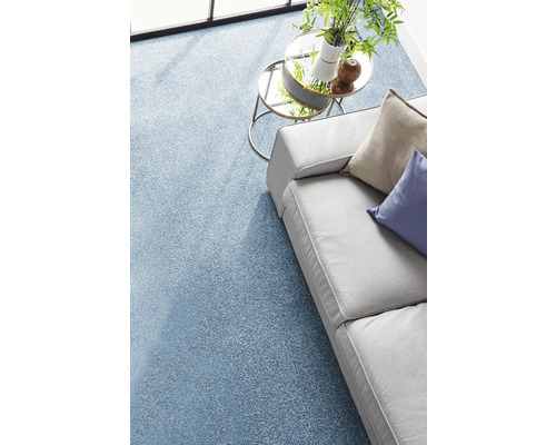 Strukturierter blauer Teppichboden in einem hellen Wohnzimmer mit grauem Sofa und gläsernem Beistelltisch.