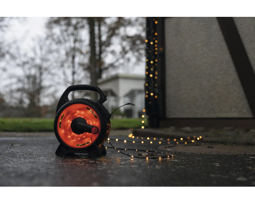 LED-Lichterkette auf schwarzer Trommel für den Außenbereich mit warmweißem Licht auf einem nassen Boden neben einem Gebäude.