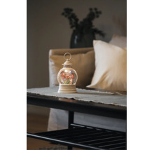 Lanterne boule à neige blanche lumineuse avec grande roue et sapin de Noël sur une table dans un salon clair et ordonné.