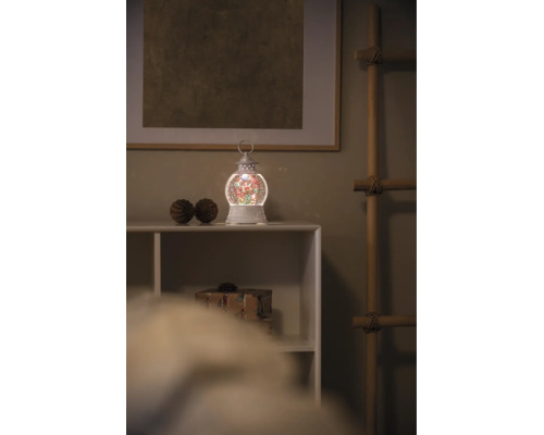 Lanterne de Noël à eau avec éclairage LED et paillettes sur une étagère blanche dans une ambiance de Noël.