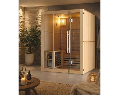 Innensauna aus Holz mit Glasfront und Glastür in einem hellen Wellnessraum mit Natursteinwand, Zimmerpflanze und Saunazubehör.