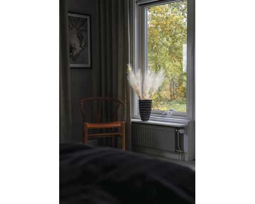 Décoration d'herbe de la pampa à LED dans un vase noir sur un rebord de fenêtre à côté d'une chaise en bois et de rideaux.