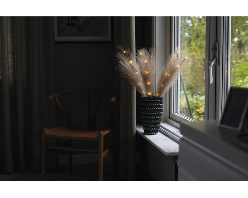 Herbe de la pampa artificielle avec éclairage LED dans un vase texturé sur un rebord de fenêtre.
