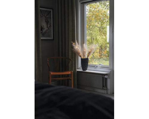 Ambiance intérieure avec chaise en bois et décoration de rebord de fenêtre en herbe de la pampa dans un vase texturé avec guirlande.