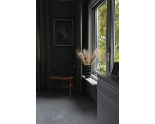 Herbes de pampa lumineuses dans un vase sur un rebord de fenêtre à côté d une chaise en bois dans une pièce chaleureuse.