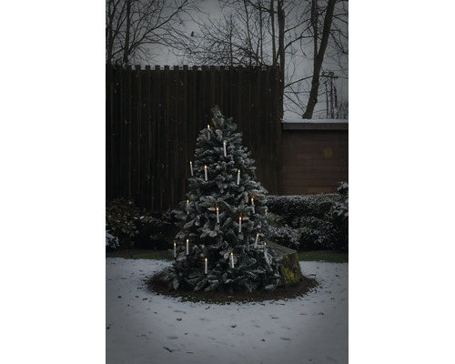Verschneiter Weihnachtsbaum im Aussenbereich mit leuchtenden kabellosen LED Kerzen in einem winterlichen Garten.