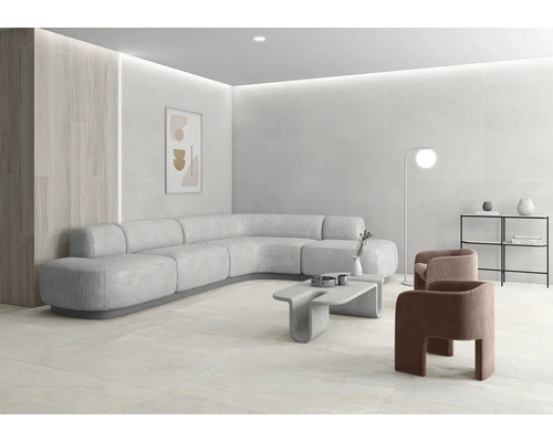 Salon moderne et lumineux avec de grands carreaux au mur et au sol, canapé d angle incurvé, table en béton et décoration minimaliste.