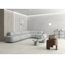 Salon moderne et lumineux avec de grands carreaux au mur et au sol, canapé d angle incurvé, table en béton et décoration minimaliste.