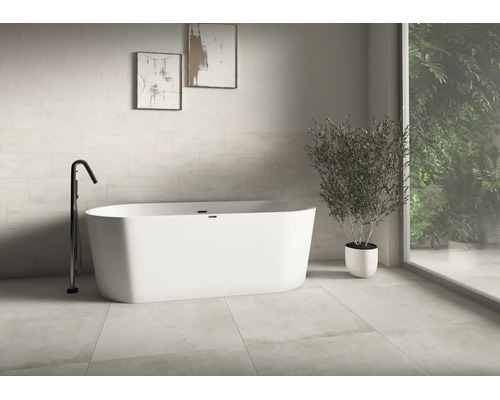 Salle de bains moderne et lumineuse avec une baignoire îlot ovale, un robinet noir sur pied, de grands carreaux et une grande plante.