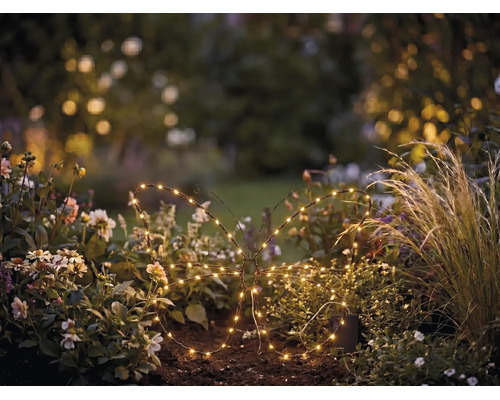LED-Gartenstecker in Schmetterlingsform mit warmweißen Lichtern in einem Blumenbeet platziert.
