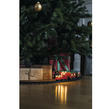 Train de Noël sur rails sous un sapin décoré avec des cadeaux sur un sol en bois.