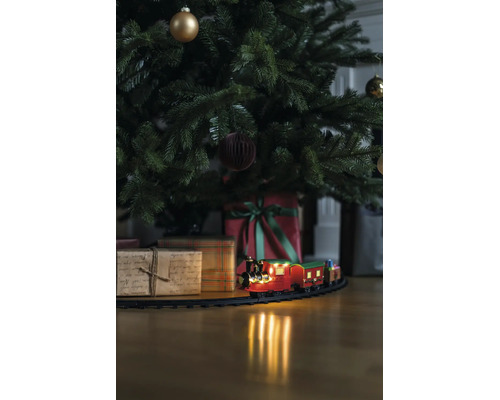 Train de Noël sur rails sous un sapin décoré avec des cadeaux sur un sol en bois.