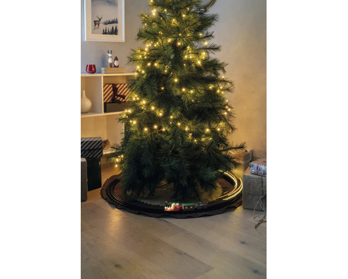 Sapin de Noël artificiel avec lumières LED et un petit train sur des rails en dessous, entouré de cadeaux.