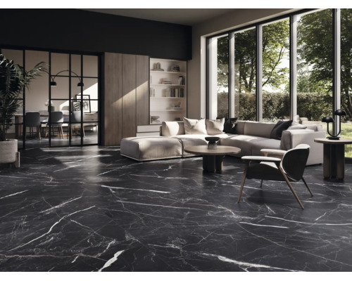 Salon moderne avec carrelage de sol sombre aspect marbre et veinures blanches, canapé clair et grandes baies vitrées.