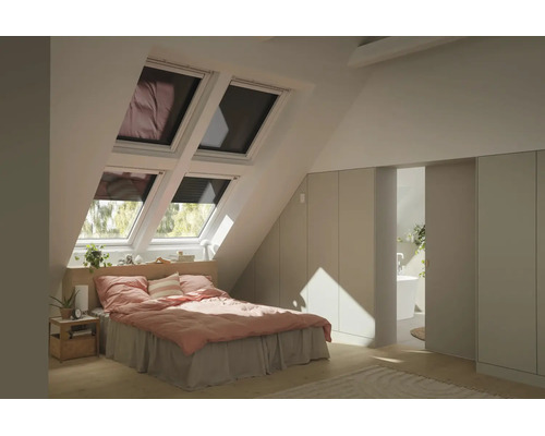 Chambre lumineuse sous combles avec quatre fenêtres de toit, lit avec linge rose, armoires encastrées et vue sur une salle de bains.