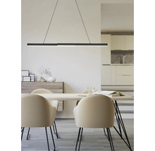 Espace repas moderne avec suspension noire au-dessus de la table en bois et chaises beiges. Buffet et cuisine ouverte en arrière-plan.