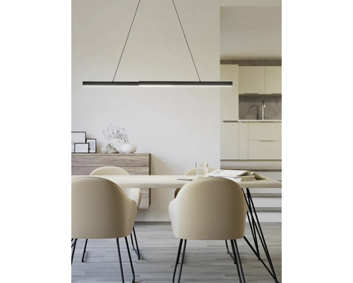Espace repas moderne avec suspension noire au-dessus de la table en bois et chaises beiges. Buffet et cuisine ouverte en arrière-plan.