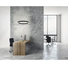 Bureau moderne avec une suspension circulaire au-dessus du bureau en bois, un mur aspect béton et une grande fenêtre dans une pièce lumineuse.