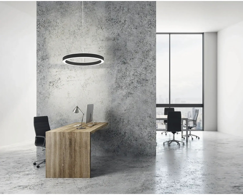 Bureau moderne avec une suspension circulaire au-dessus du bureau en bois, un mur aspect béton et une grande fenêtre dans une pièce lumineuse.