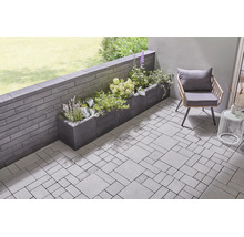 Terrasse moderne avec pavés, mur de jardin en blocs de béton et un bac à plantes fleuri.