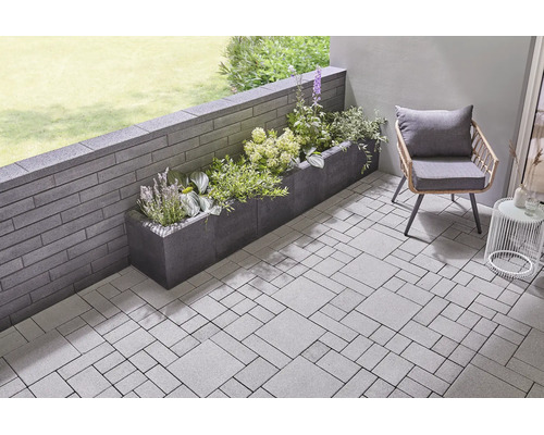 Terrasse moderne avec pavés, mur de jardin en blocs de béton et un bac à plantes fleuri.