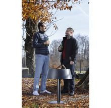 Zwei Männer stehen im herbstlichen Garten an einer modernen, brennenden Feuerschale aus Metall und unterhalten sich.